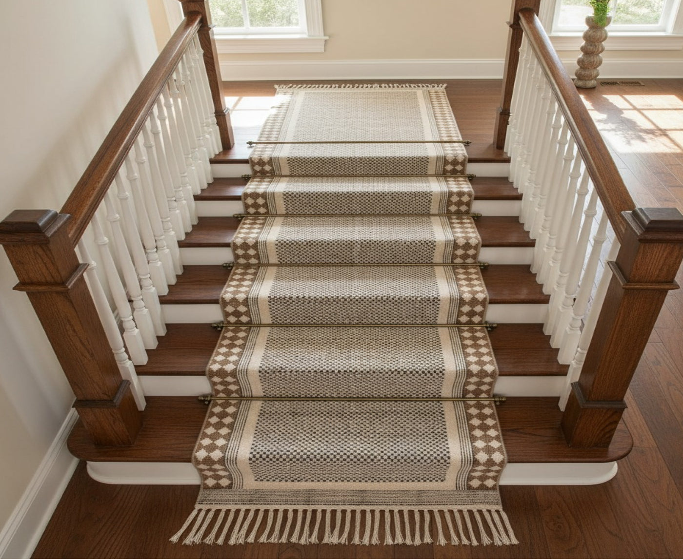 A woven stair runner with fringe and geometric patterns draped over a wooden staircase with white balusters.