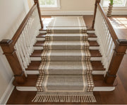 A woven stair runner with fringe and geometric patterns draped over a wooden staircase with white balusters.