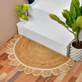 A semi-circular natural jute entry rug with a scalloped edge, styled on a wooden floor in front of white stairs with potted plants.